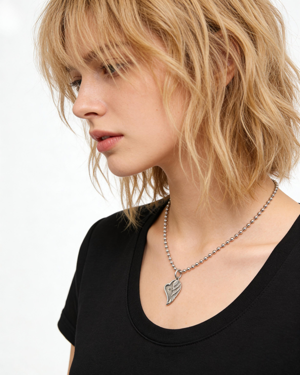 Woman wearing a black top and a necklace with a angel heart wing pendant on a white background