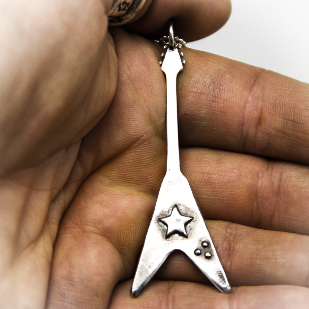 silver flying v guitar pendant in hand. 