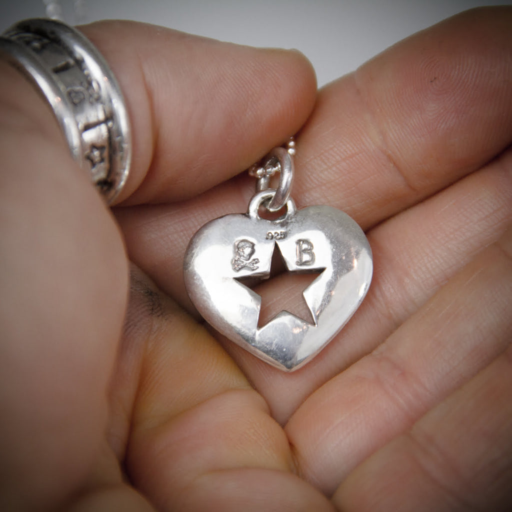 a hand holding a silver heart pendant showing back side and makers mark.