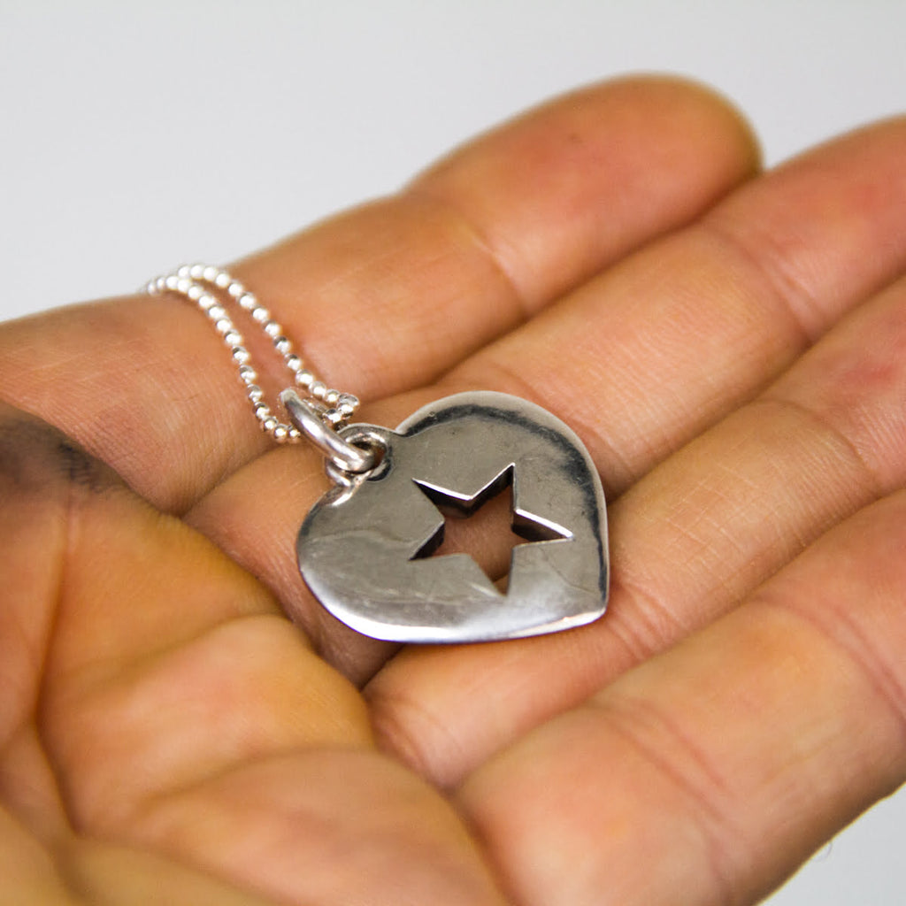 Silver necklace with a heart-shaped pendant featuring a star design held in a hand.