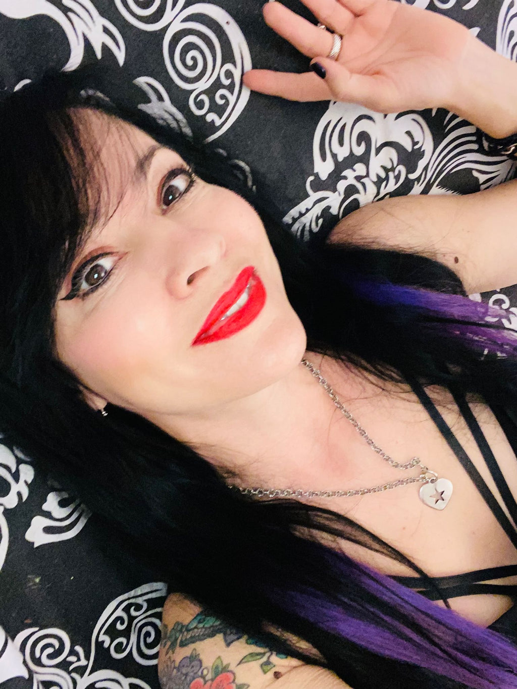 Person with red lipstick and tattoos wearing a rockstar heart pendant against a colorful background.