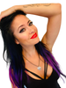 Woman with purple hair and red lipstick wearing a skull guitar pic pendant on white background. 