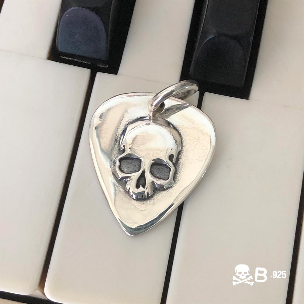 Guitar Pic Skull pendant laying on piano keys.