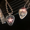 a pair of guitar pic pendants with stars on them with chains on a guitar. 