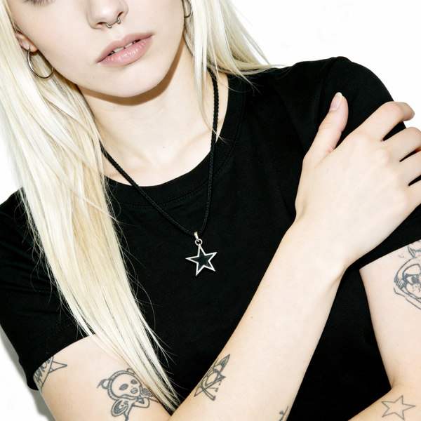 Person wearing a black t-shirt with a star pendant necklace, surrounded by tattoos.