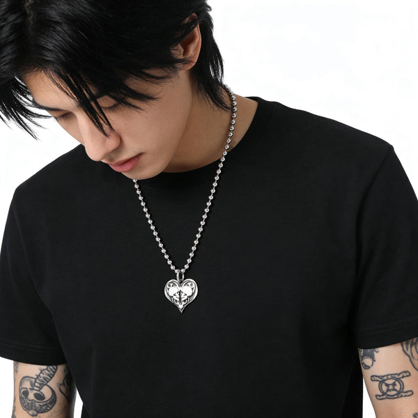 Person wearing a black t-shirt with a silver chain necklace featuring a true love double skull heart pendant.
